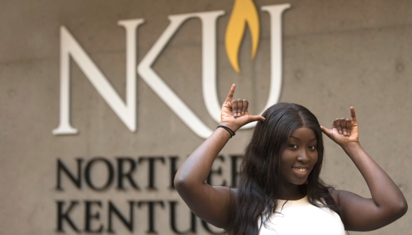 Black female student standing in front of the ɫƬ logo giving a Norse Up